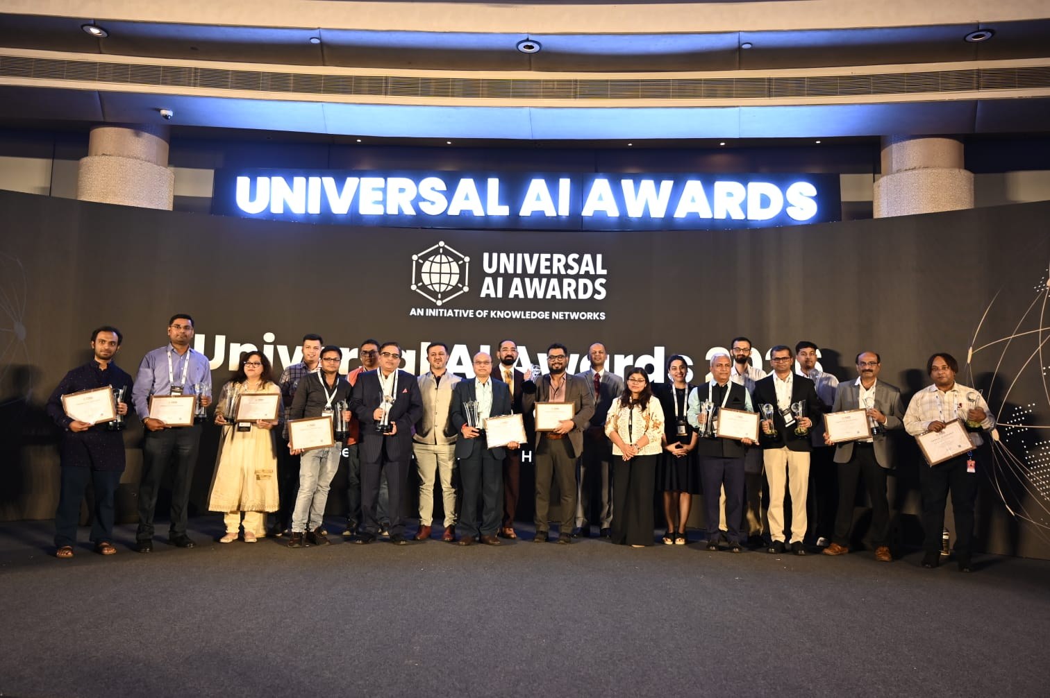 All winners of the Universal AI Awards 2026 India Chapter standing on stage with their certificates under the awards sign